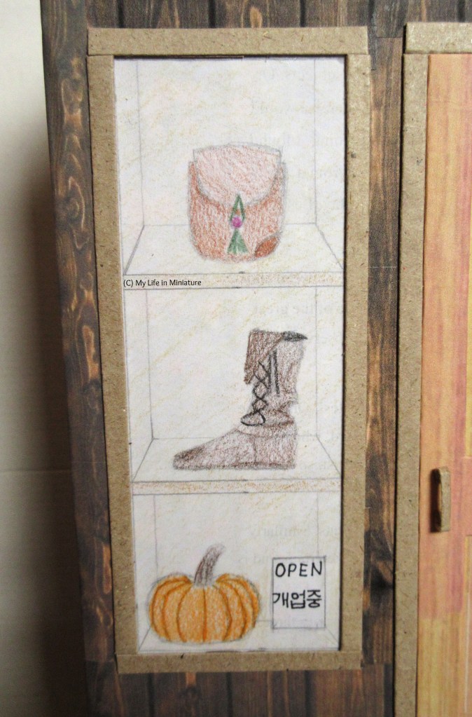 Close-up of the left-hand window. Both the windows and the door are framed in a slightly darker wood. The bottom of three shelves has an 'Open' sign inside, in English and Korean. 