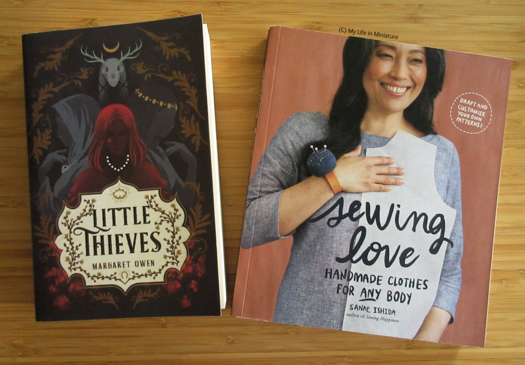 Two books ('Little Thieves' by Margaret Owen and 'Sewing Love' by Sanae Ishida) are laid flat next to each other on a wood background. 