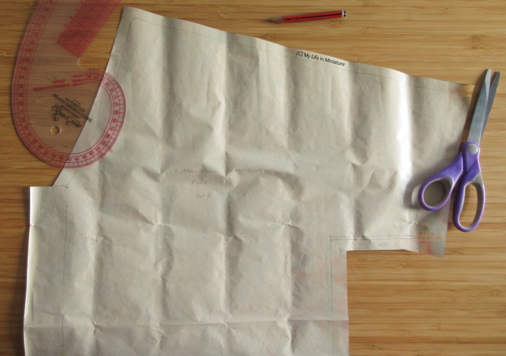 The top half of a simple shirt pattern is pictured on a wood surface. Around it is a French curve ruler, a pencil, and a pair of paper scissors. 