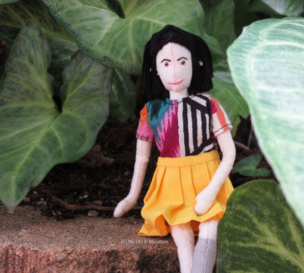 Tiffany sits on a rock ledge, underneath the leaf canopy. She faces the camera, one hand behind her and one hand in her lap, smiling. 