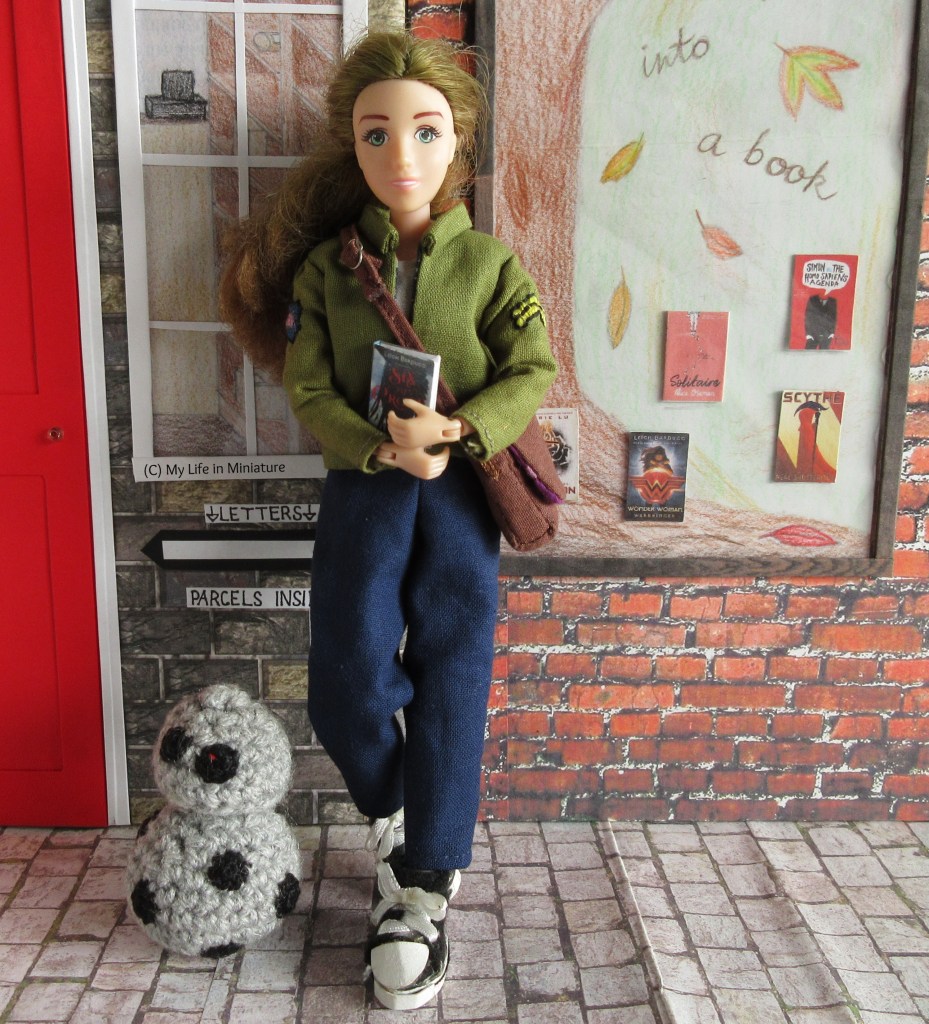 Sarah leans against the wall between the Post Office and the Palace Library. She wears the same outfit as before, Chip near her feet. One foot is tucked behind the other as she smiles at the camera. 