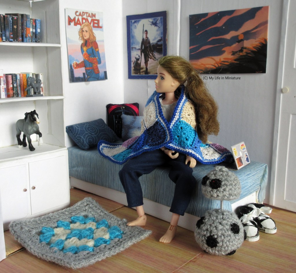 Sarah sits on her bed, both legs to one side, and surveys the room. The blanket is now over her shoulders as a cape; her jacket has been cast off somewhere. Chip is beside her now, head still raised in surveillance. 