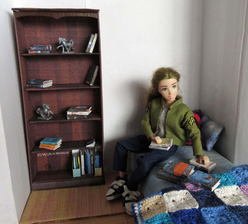 Sarah sits on her bed, looking at the books on it. She's made a few piles on the bed, and has her hands resting on one each. The bookshelf is still in a state of disarray, though slightly less than before. 