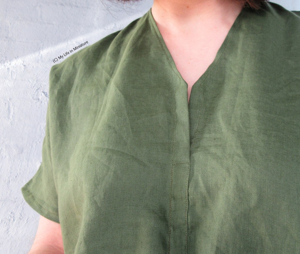 Closeup of the V-neckline of the shirt. The shirt is sewn closed at the centre front, with a small amount at the top unsewn. The neckline sits quite close to the neck, with nothing showing through the unsewn bit.