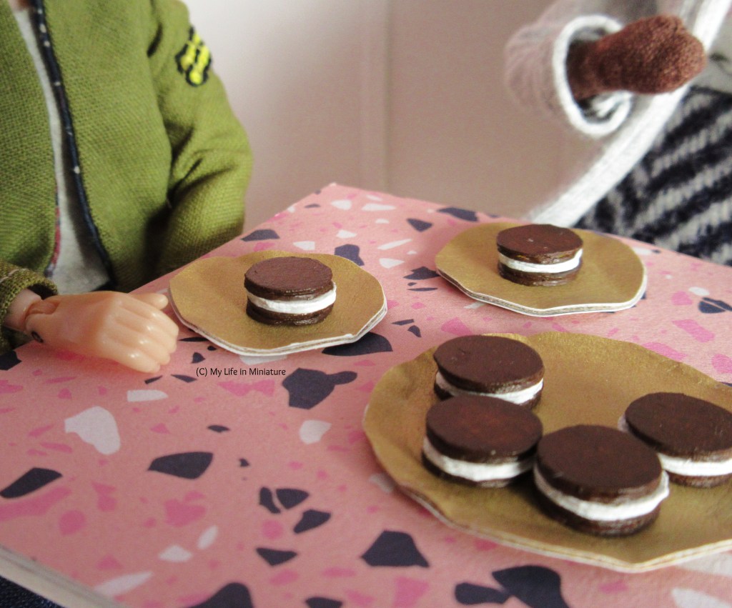 Another close-up of the pastries on the table. This time there are four on the serving plate, with two on smaller dessert plates. One plate sits in front of Sarah, the other in front of Hazel. 