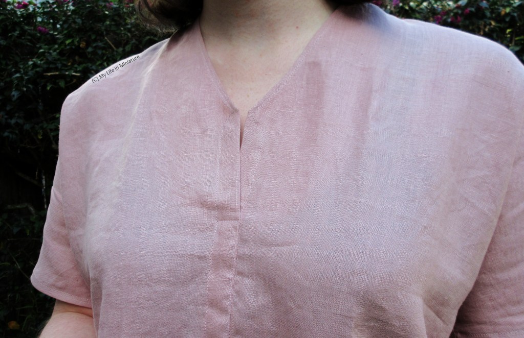 Close-up of the V-neck of the pale pink top. The V-neck sits high on the chest, with a split in the centre front seam a bit below the base of the V. 