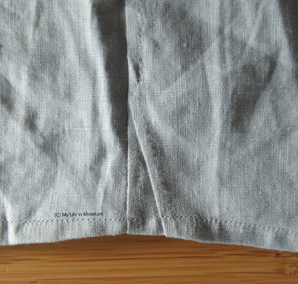 Close-up of the linen shirt, laid on a wood surface. Close-up shows the side seam of the shirt at the hem edge, where there is a triangle of fabric inserted. 