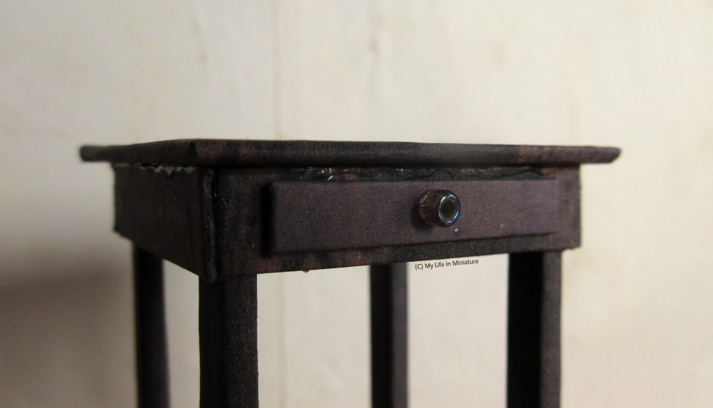 Close-up of the small table, at a different angle. This angle highlights the drawer on the front, which has a single circular handle in the middle of the drawer. 