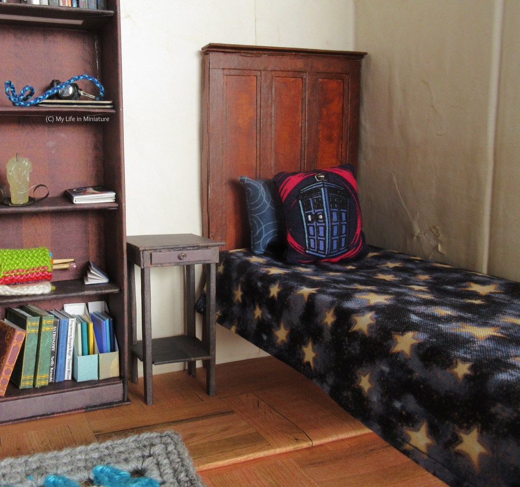 Interior of Sarah's bedroom; in particular, Sarah's bed is centre of frame with her bookshelf to the left of the image. In-between the bed and the bookshelf is a small, dark wood table, just a bit taller than the bed. 