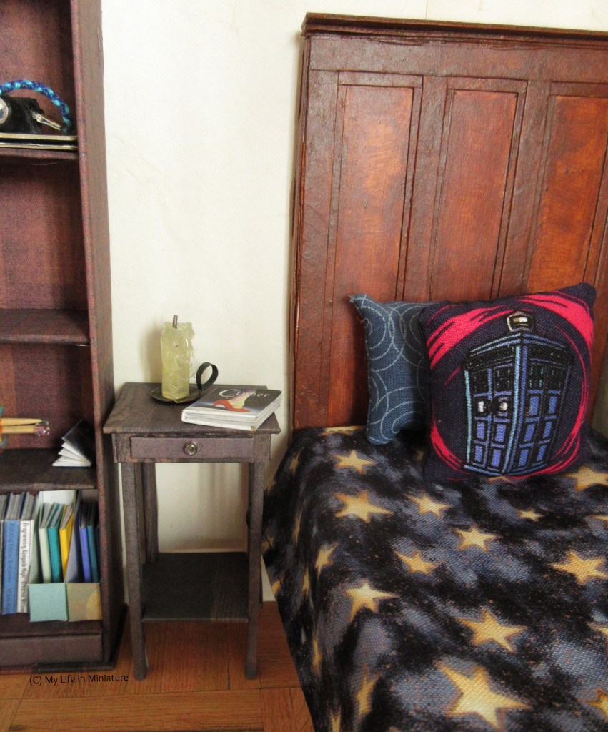 Close-up of the bedside table in its position, with the candle and the novel on top. Sarah's bed is to the right of the image, and her bookshelf to the left. 