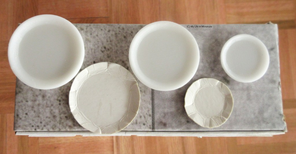 Five white plates are photographed from above on a stone surface. They are arranged in a zigzag; the top three plates have been 3D printed, and the bottom two have the creases of paper. They are of varying sizes; the largest being on the top left, with the middle two being slightly smaller, and the two on the right the smallest. 