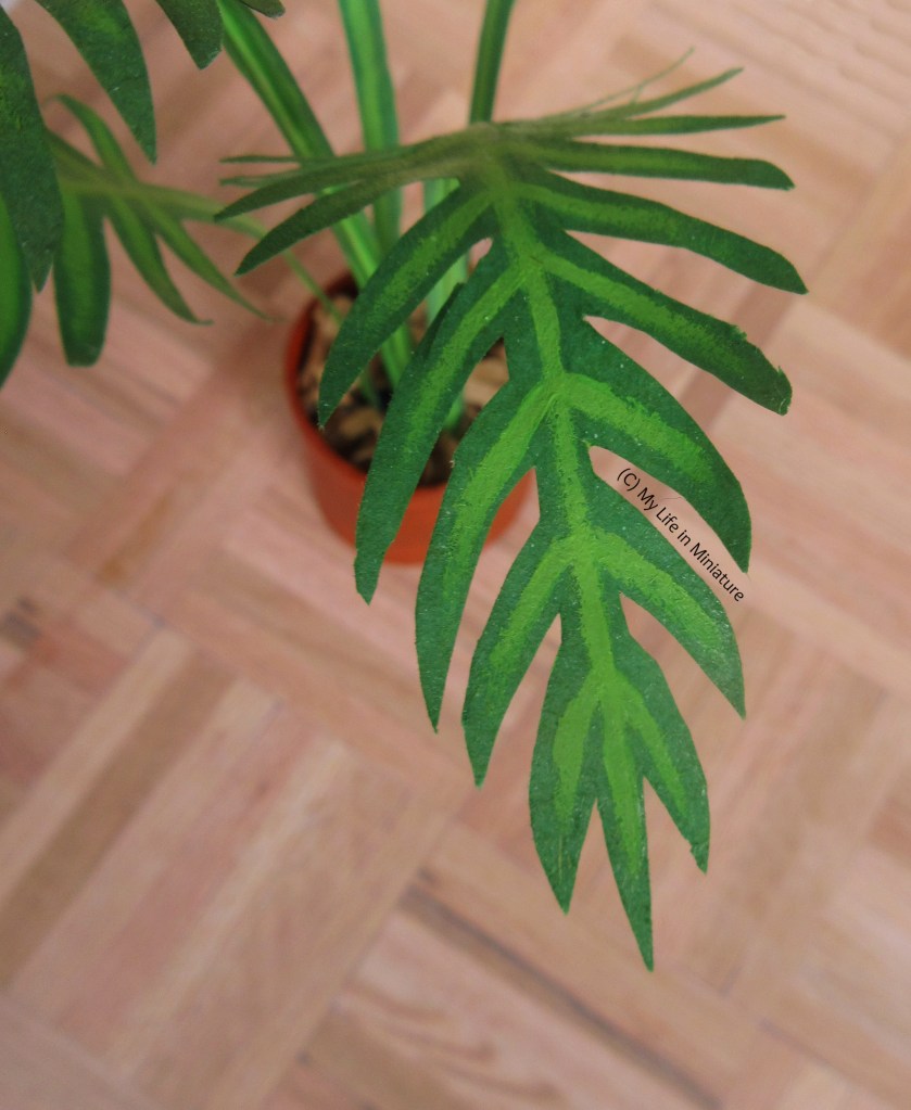 Close-up of the tip of one of the leaves. Down the centre of the leaf, and down each frond, is painted a paler green line. 