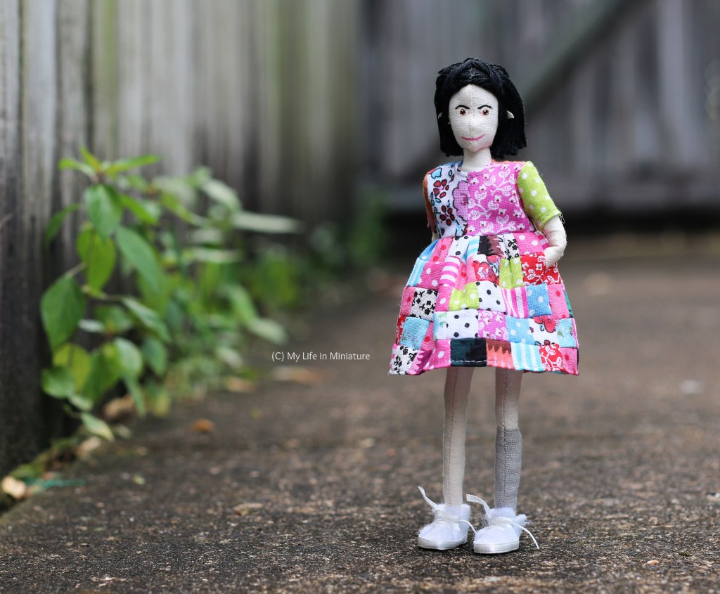 Tiffany faces the camera again in her patchwork dress, smiling at the camera. She has her hands in the in-seam pockets of the dress. 