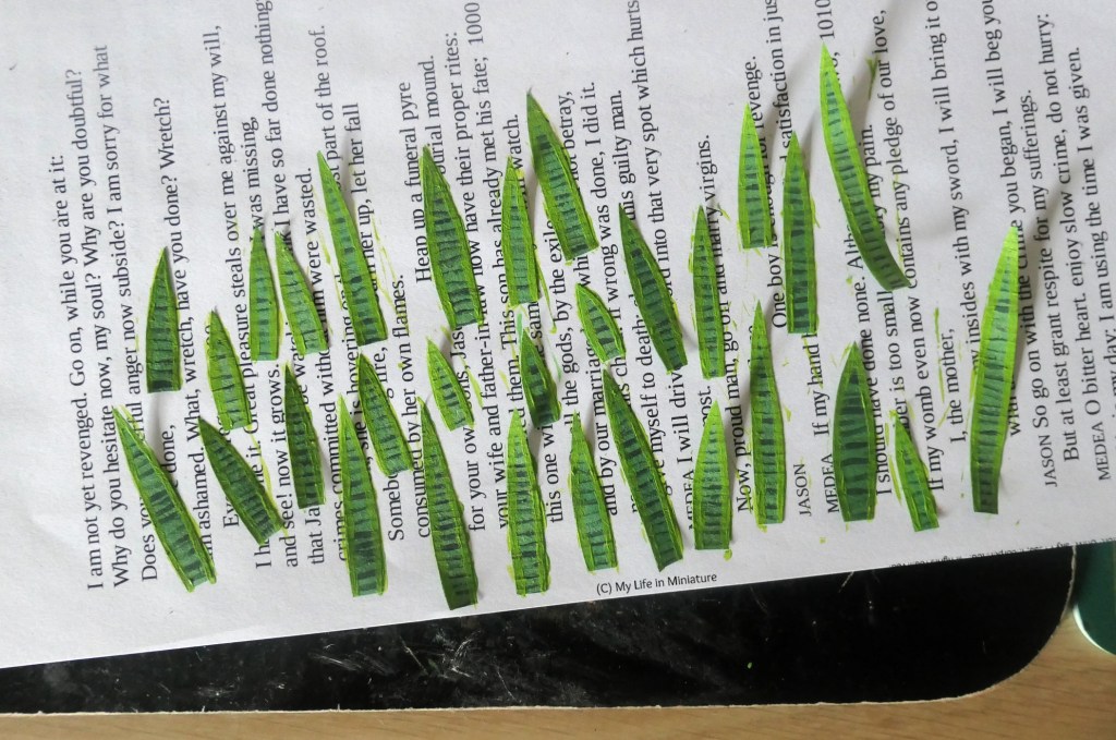 A good 30-odd miniatire paper leaves rest on a piece of scrap paper, curled with the application of paint. They are reminiscent of snake plant leaves, being pointy with dark horizontal stripes and lighter green edges. 