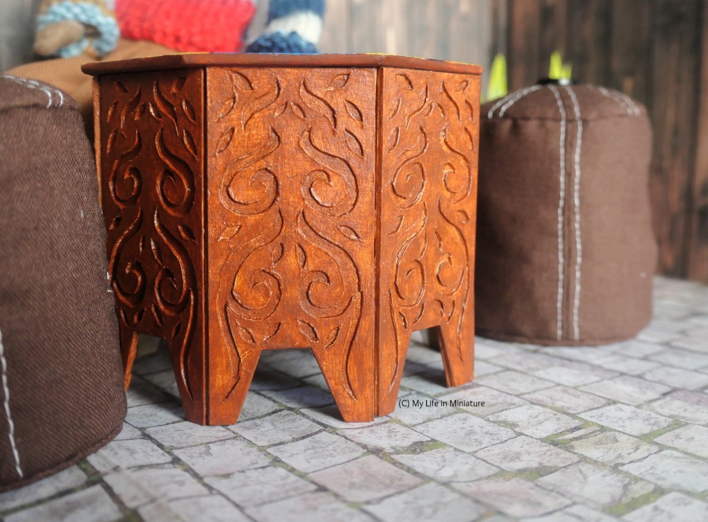 Close-up of the legs of the table. The relief carved into the legs is a leafy, spirally, organic design, that is symmetrical. Each of the eight legs has the same design, and they are all painted to look like wood. 