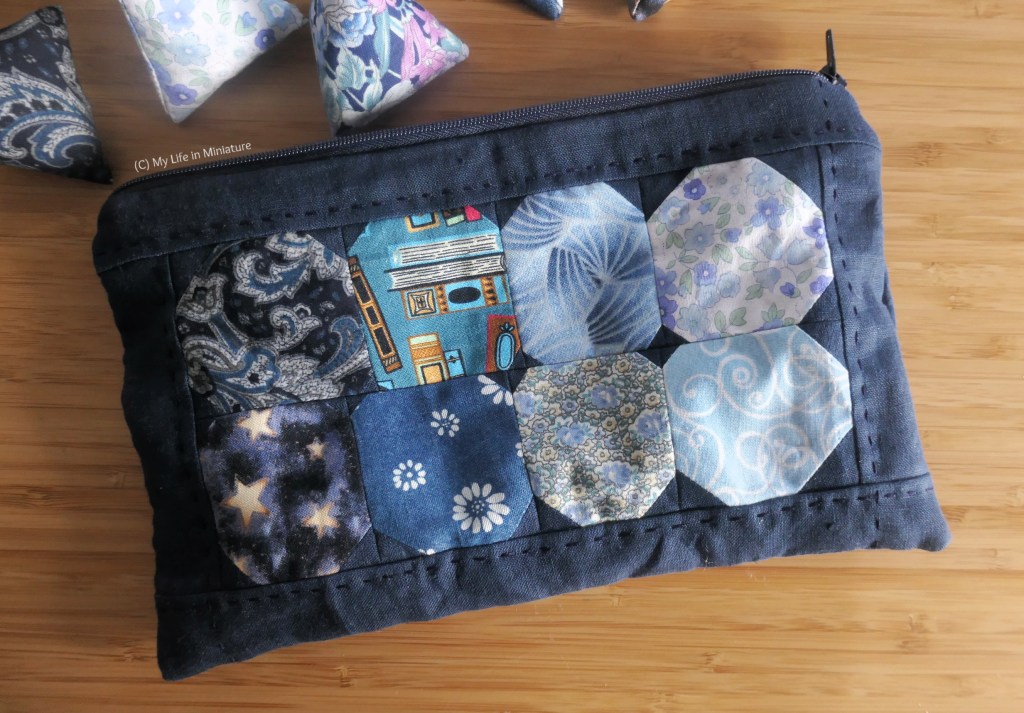 Close-up overhead shot of the pouch. The patchwork design is two rows of four circles in the centre, bordered by navy linen. The circles are in eight different blue fabrics, roughly ranging from darker to lighter across the pouch.