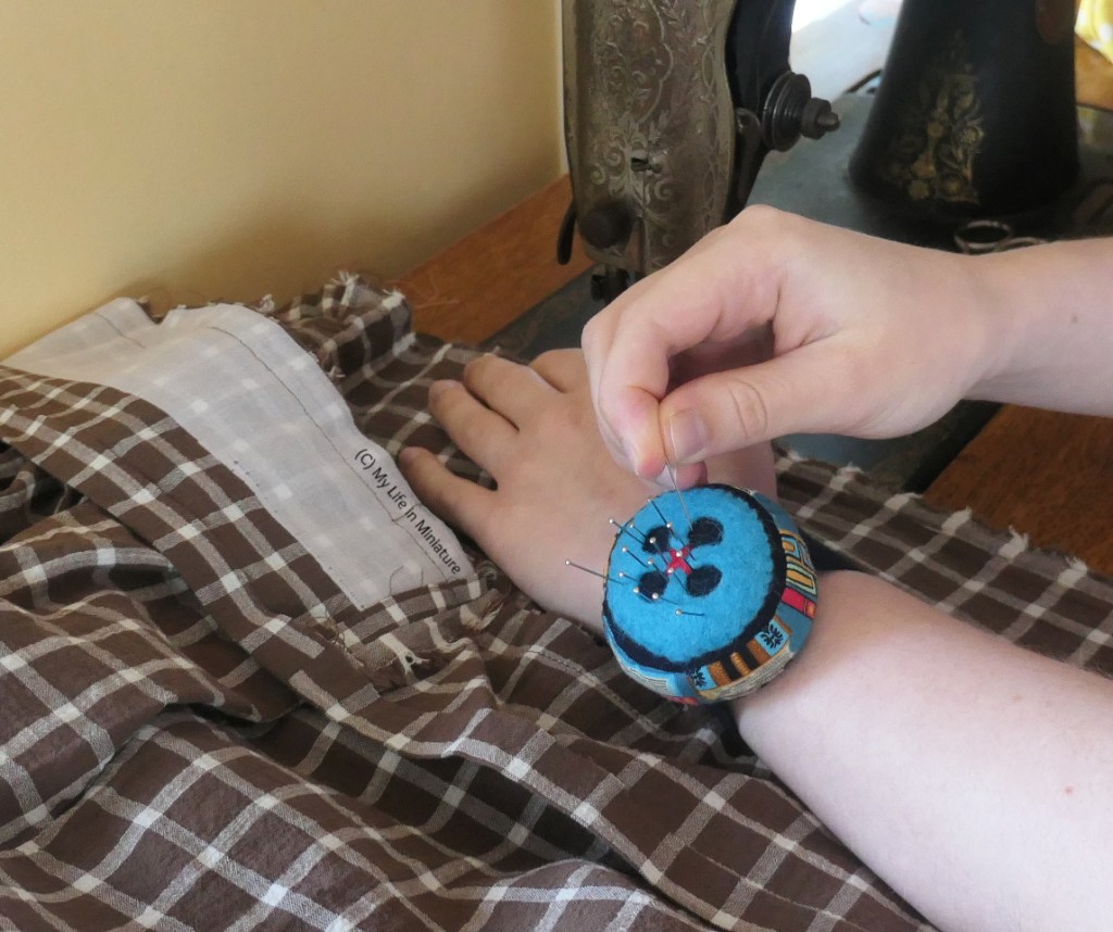The author is sewing at an old sewing machine, again photographed so only her lower arms are visible. She's in the act of putting a pin into the pincushion while the machine is stopped. 