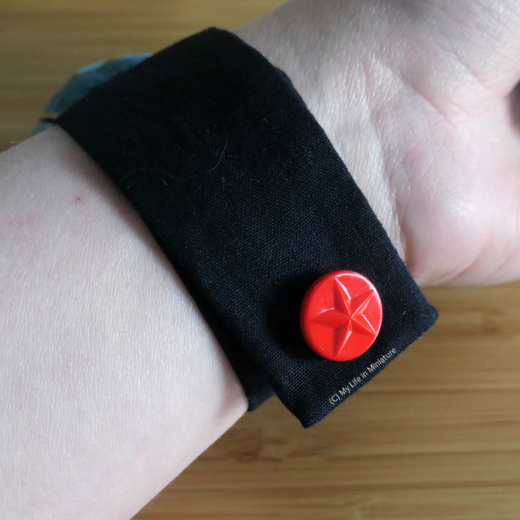 Close-up of the closure of the pincushion, closed around the author's wrist. The velcro is not visible, because it is under the red button that is visible. 