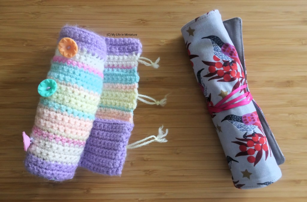 The author's old and new hook rolls are beside each other on a wood background. The old crocheted one is to the left, and the new fabric one is on the right. They are both rolled up, the fabric one tied shut and the crohet one more loosely. 