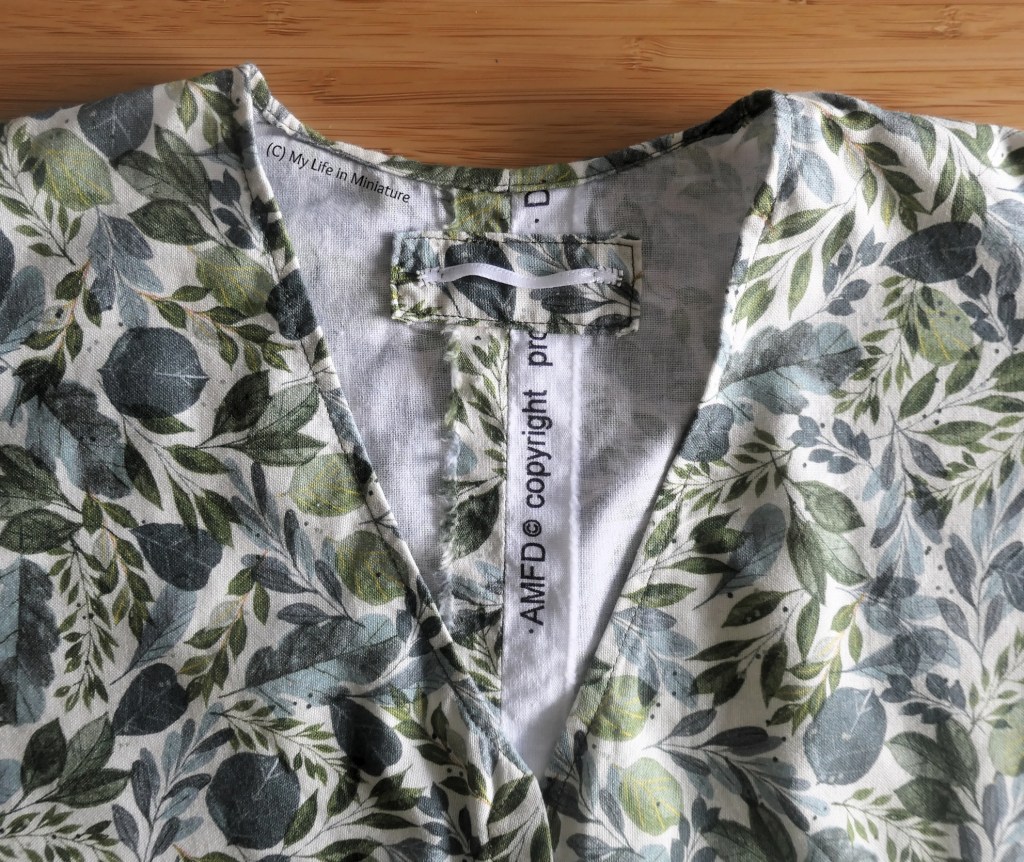 Close-up of the neckline of the leafy shirt, taken from above on a wood surface. The centre back seam allowances are visible, where a rectangle of matching fabric with a hanging loop has been sewn over top. 