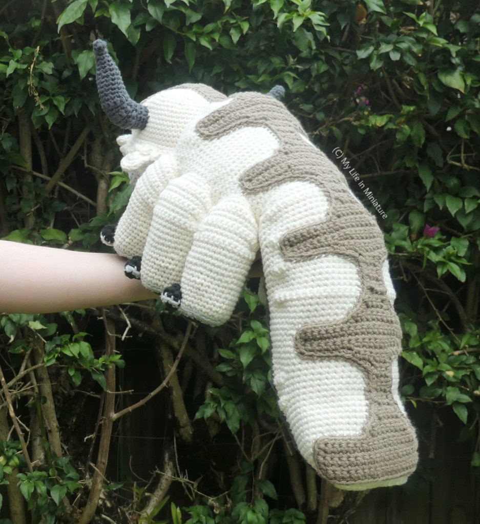 Back view of the toy, also in front of the hedge. The brown back markings are more visible now, and extend down the sky bison's back and tail. 