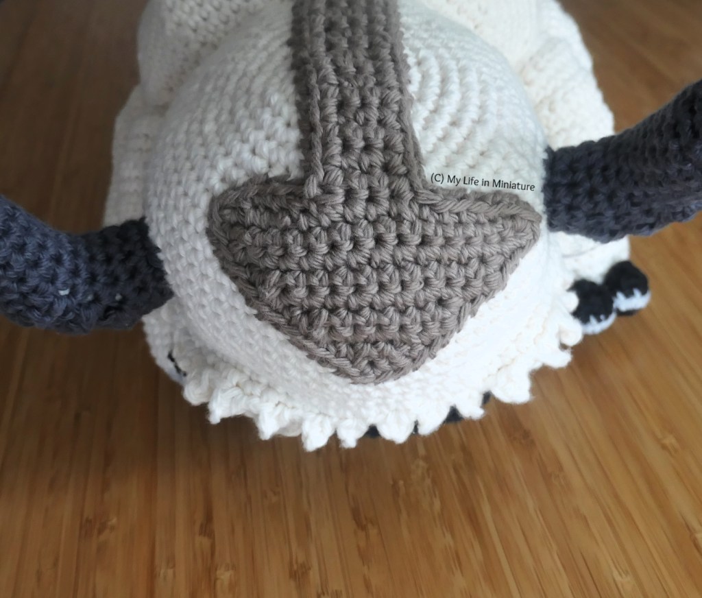 Close-up of the top of the toy's head, on a wood surface. The brown markings are in the shape of a downward-pointing arrow, between the two horns. 