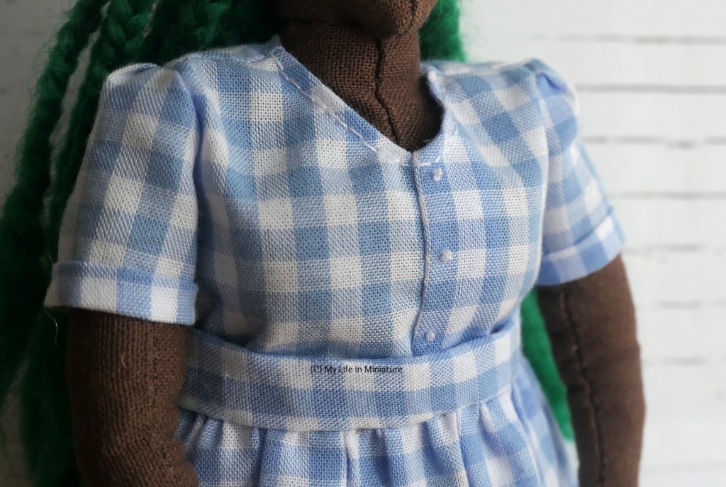 Close-up of Hazel's top. Focus is on the centre front, which has a fold and three small white knots to look like buttons. The top has a V-neckline, and the sleeves are fairly snug against her arms. 