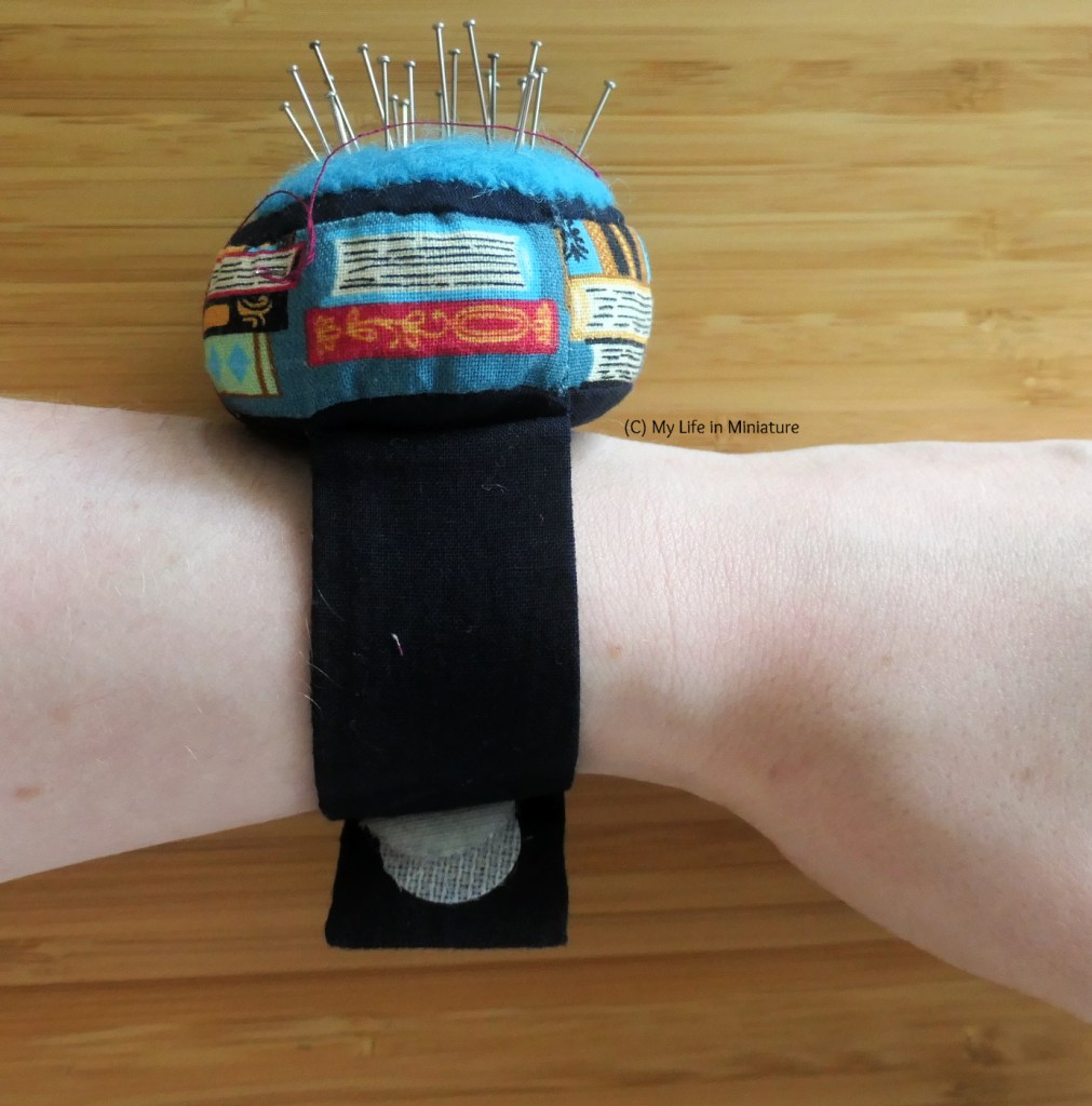 Close-up of the author's wrist, wearing a handmade wrist pincushion. The cushion's sticky Velcro closure at the bottom is peeling away from the fabric. 