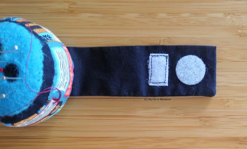 Close-up of the wrist pincushion's strap, laid flat on a wood surface. The piece of sticky Velcro has been replaced with a rectangle of sew-on Velcro in the same place. 