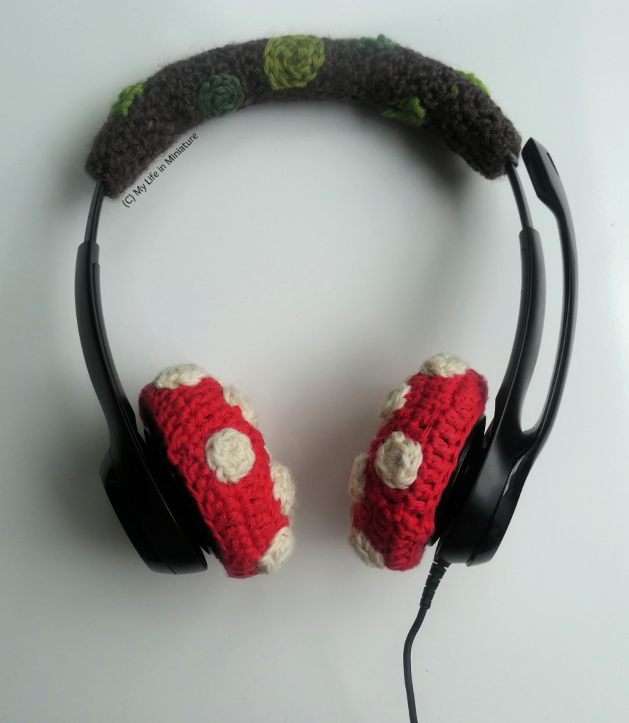 The whole set of headphones, with mossy log overhead cushion cover and red-and-white mushroom cap earmuff covers. It's photographed on a white background.