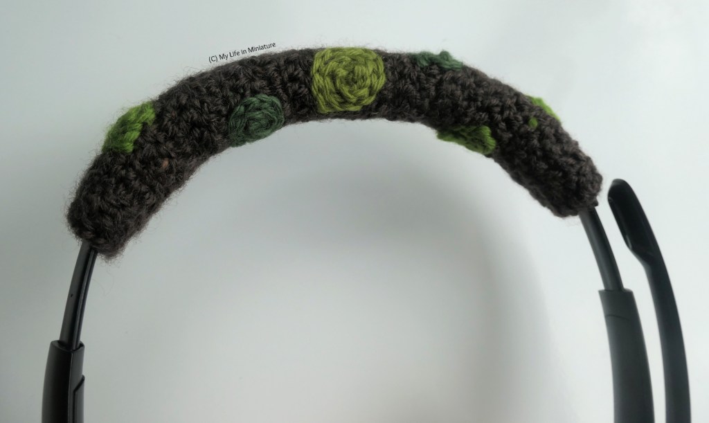 Close-up shot of the overhead cushioned area of the author's headphones. The new crocheted cover for this bit is brown, with small green circles crocheted onto the brown to look like moss. 