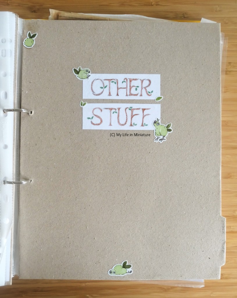 The third section divider in the binder, this time for "Other Stuff". Again, it is very similar to the first two. The tab is at the bottom right, and there are four stickers. Two are at the corners of the label, one at the centre bottom, and one in the top left corner. These stickers are of little bird-chick-like moss creatures, with leaf tails.