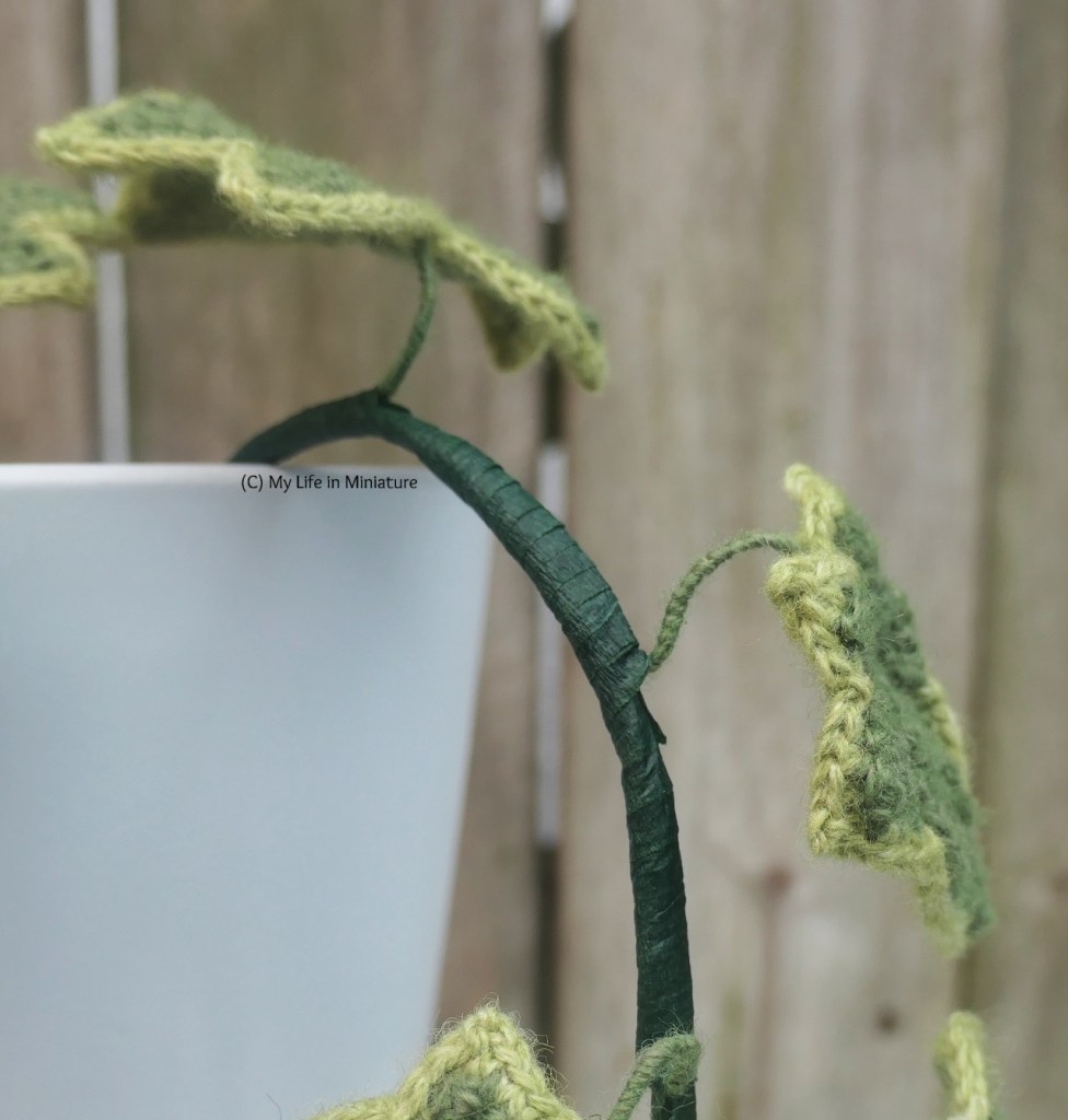 Close-up of part of one of the vines. Said vine is wrapped in dark green florists' tape, with a small piece of wire curving up to connect to the leaf. The leaf stem is wrapped in dark green yarn. 