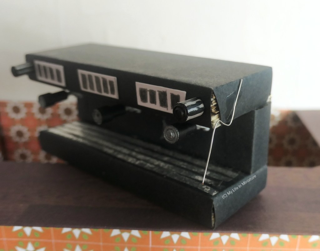 Closeup of the other end of the coffee machine, where a wire has been bent into shape and glued to the side of the machine for the steam wand. Another knob is visible, too.