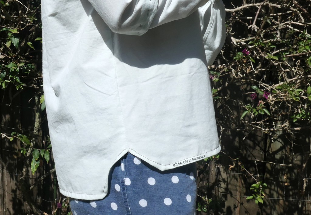 Close-up of the hem of the mint green shirt, at one of the side seams. The shirt is slightly longer at the back than the front, and the hem curves up and them back down again at the side seam. The author's hem has quite angular curves.