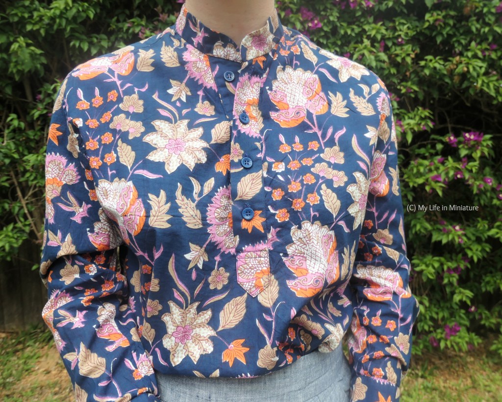 Close-up of the centre front placket of the navy shirt. The florals are easier to see; there are larger flowers in multiple colours, as well as smaller, single-coloured flowers. There are four navy blue buttons along the placket, and the bottom is pointed. 