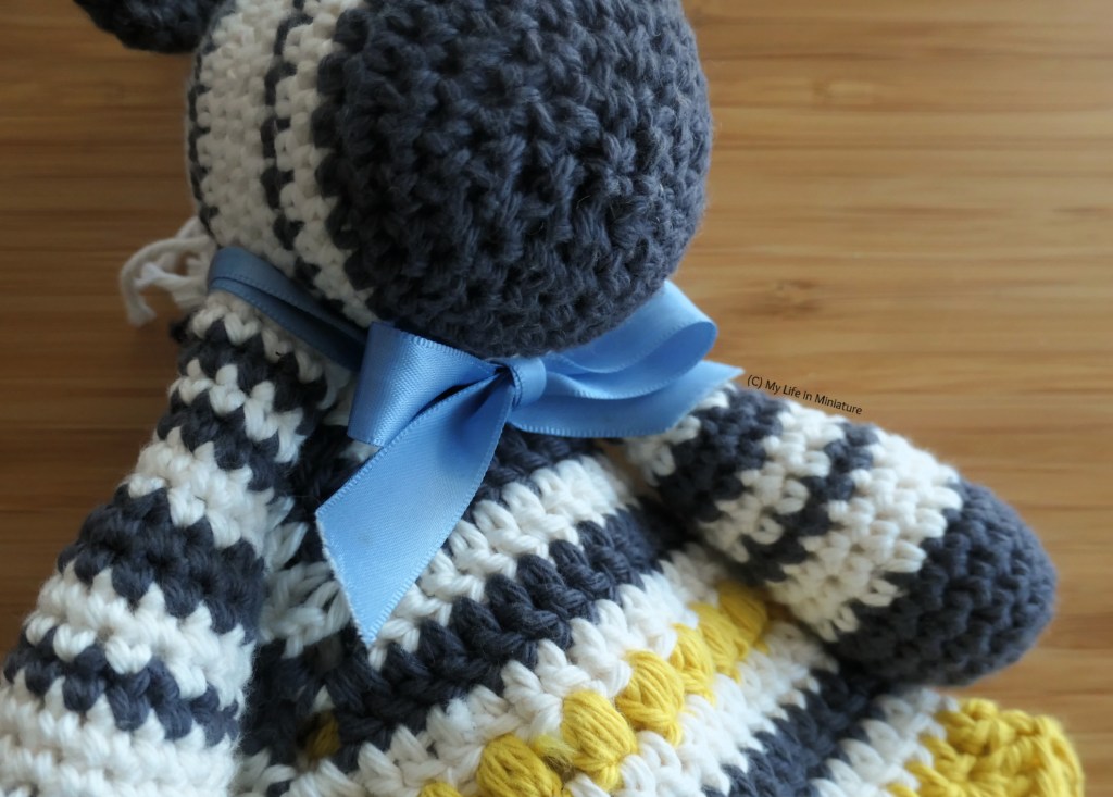 Close-up of the bow around the toy's neck. It's pale blue satin ribbon, tied in a boe under the toy's chin.