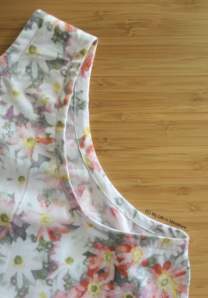 Close-up of one of the armholes of the tank top, laid flat on a wood surface. The bias binding used to finish the armhole is visible, and is the same fabric as the outside. 