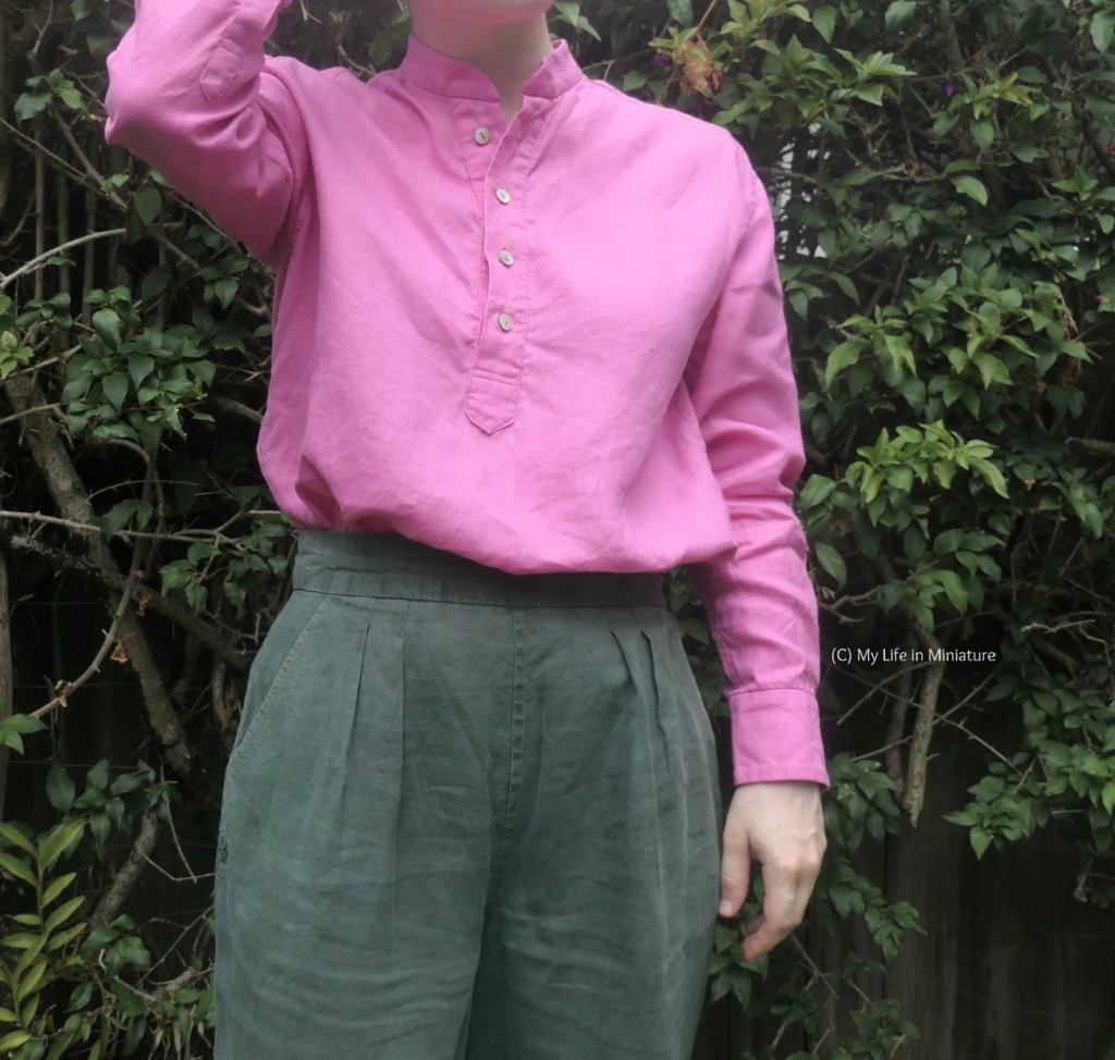 The author faces the camera again, wearing the pink shirt tucked into green pants. One arm hangs at her side, while the other is raised above the frame. 