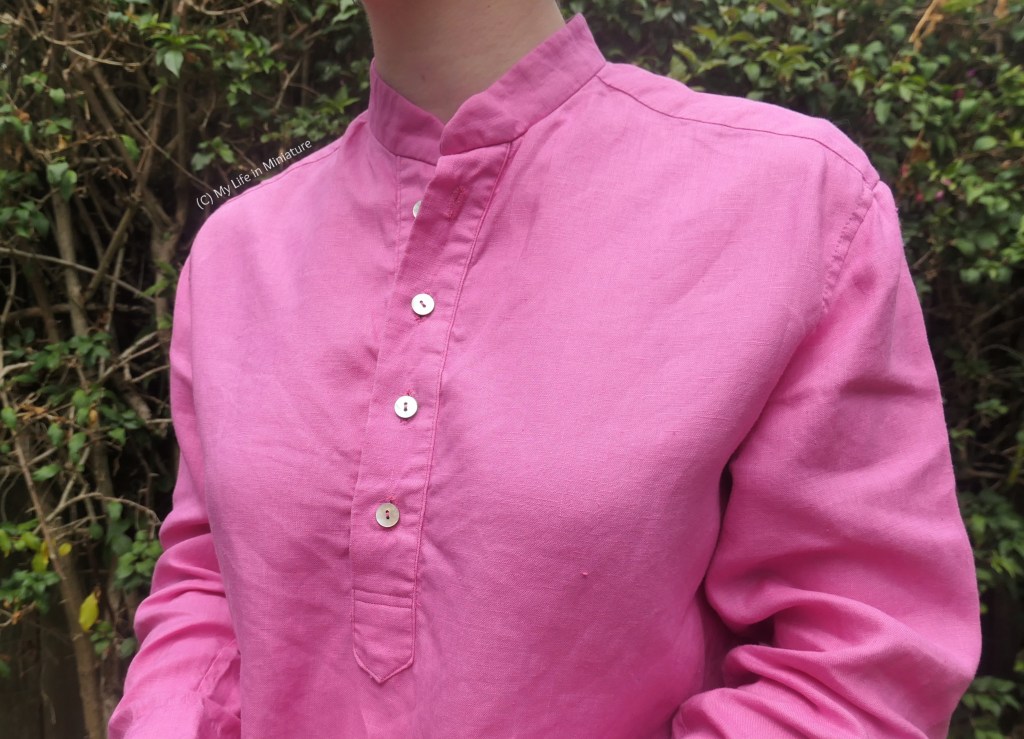 Close-up of the collar and centre front button placket of the pink shirt. The four buttons are small and shell-iridescent. Only the bottom three are buttoned closed. 