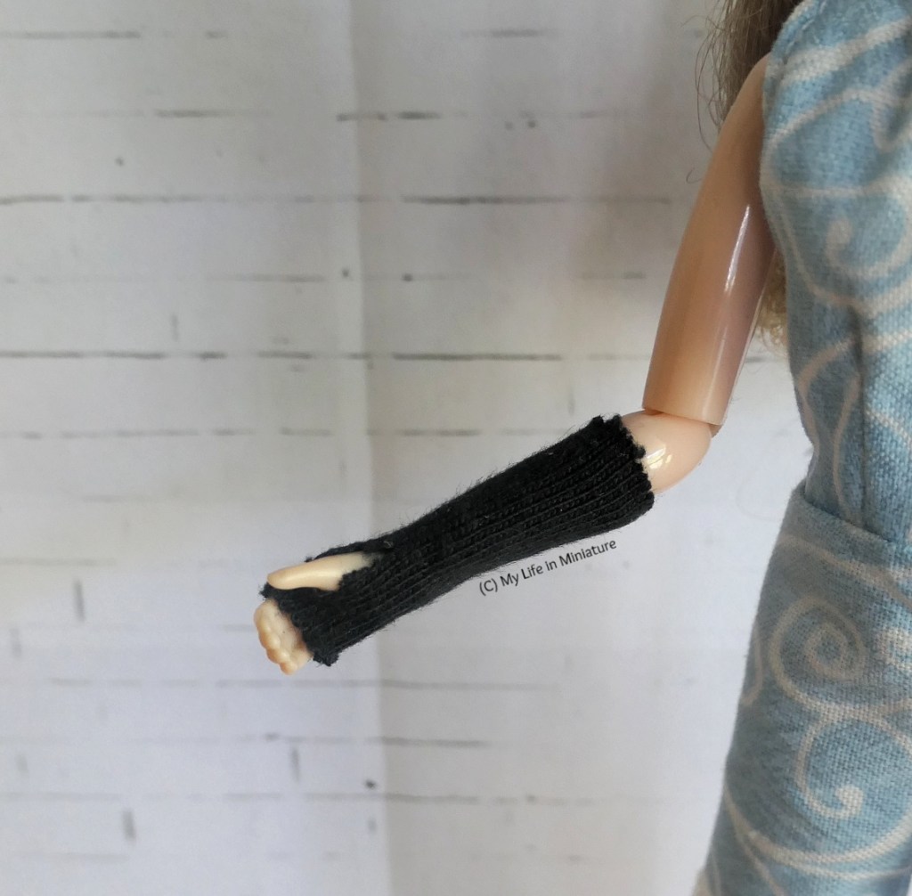 Another close-up of Sarah's right arm, however this time the inside is visible. It remains encased in the black knit tube, and the thumbhole is more visible. 