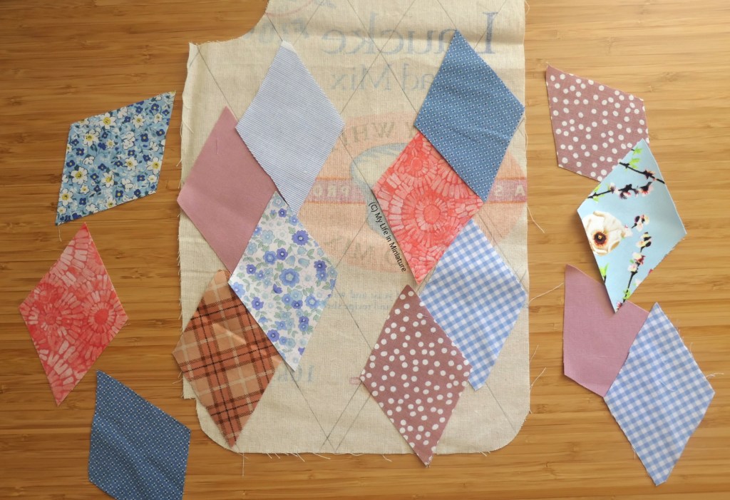 The bottom half of a jacket bodice front piece, made of calico, is flat on a wood surface. On it, and around it, are a number of the fabric diamonds from the last image. They are pink and blue, and a variety of patterns and shades, all leaning on the paler end of the spectrum.