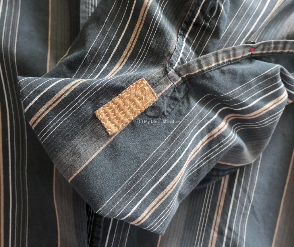 Close-up of the interior of the sleeve where the rips were. A small rectangle of tan cotton has been stitched to the shirt, and there are lines of large-ish running stitches in the panel, doen in yellow thread.