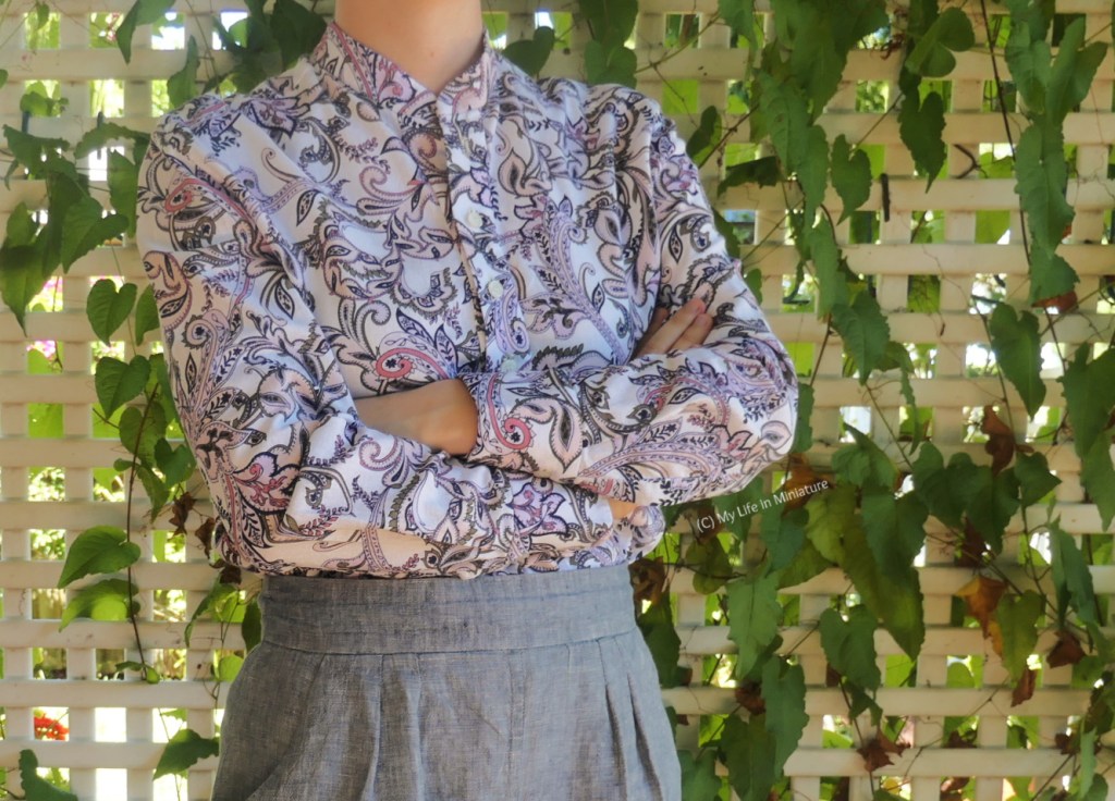 The author stands in the same place and wears the same outfit as the last image, photographed from neck to thighs. She has her arms crossed over her chest, and is at a three-quarter angle to the camera. The shirt has a collar stand, but no collar. 