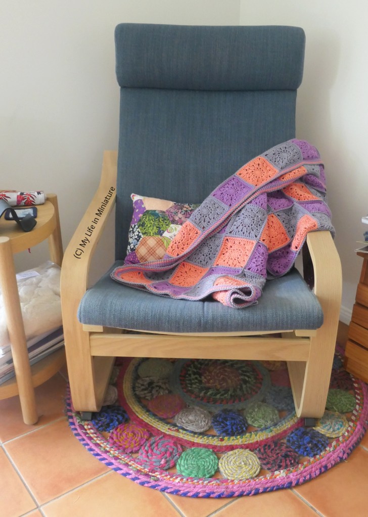 The crocheted blanket is messily draped over one arm of the armchair, mostly obscuring the hexagon patchwork cushion. 