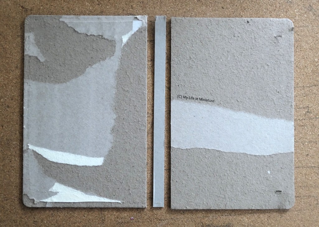 The cardboard inserts that were inside the notebook's cover are photographed from above on a cork surface. They have been stripped of their pleather and paper coverings, and are arranged to look like an open book.