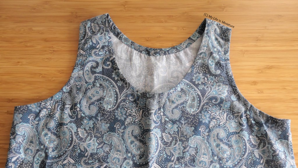 Close-up of the top half of the paisley-print top, on a wood background. It has matching bias binding sewn around the neck and armhole edges, so the raw edges there are finished.