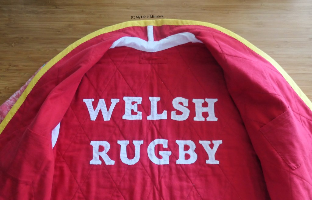 Close-up of the inside of the back of the jacket, from about waist up. The jacket is lined in red fabric, and across the back are the words "WELSH RUGBY", appliqued on in white fabric. The internal seams have also been bound in white bias binding, and there is an (almost invisible) hanging loop just under the collar.