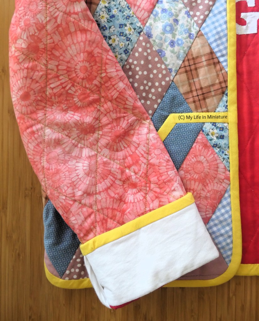 Close-up of the sleeve and one front panel of the quilted jacket. The sleeve has been quilted in a diamond pattern to match the diamonds on the bodice. The white cuff is unquilted, and all the edges (of the jacket, cuff, pocket) have been bound with yellow bias binding.
