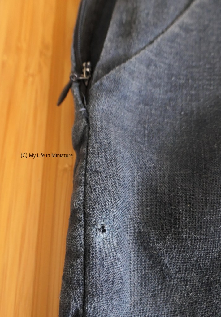 Close-up of the side seam of a pair of navy pants. A hole has worn through the outside fabric, a little below the pocket opening and the base of the zip.